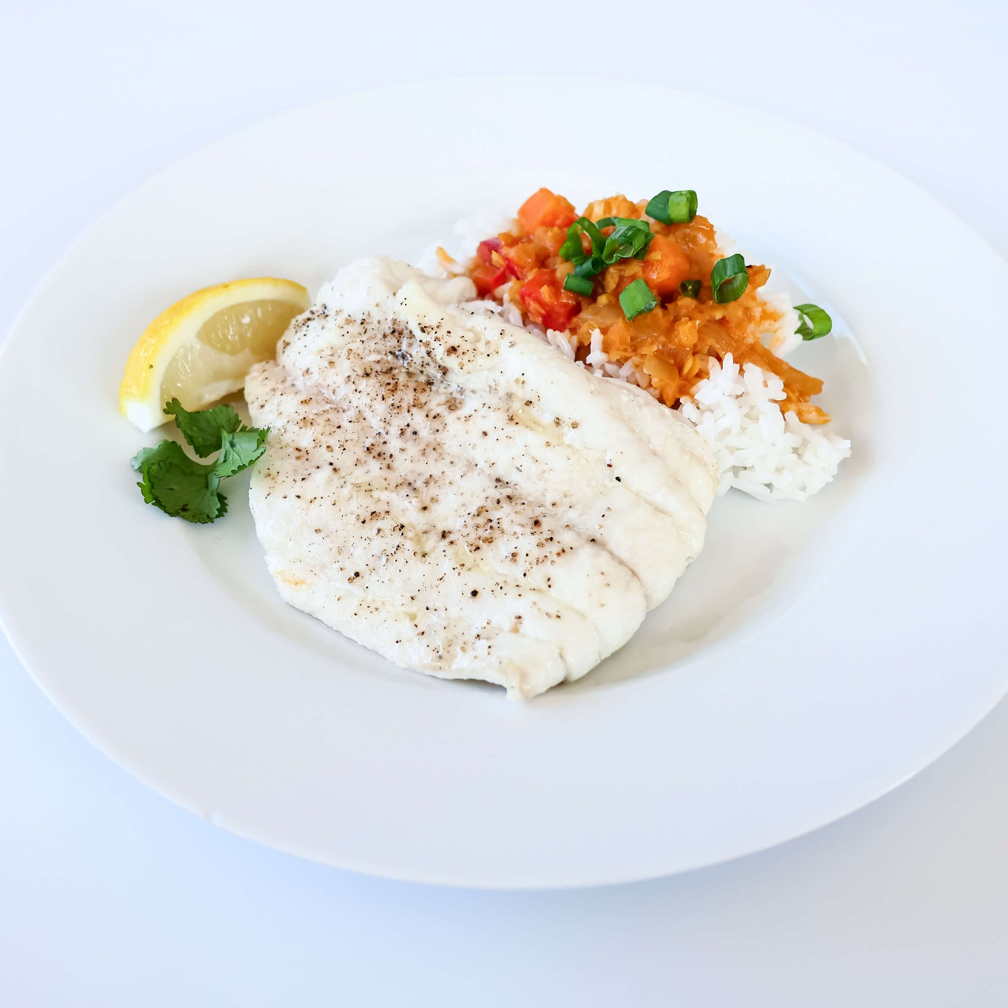 oven baked haddock on a white plate with rice, vegetables, and a lemon wedge